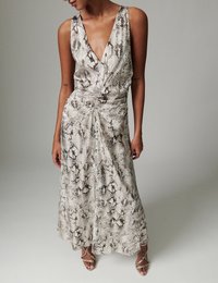 Γυναίκα που φοράει αμάνικο midi φόρεμα με V-λαιμόκοψη και ραβδώσεις, με μπεζ και καφέ φίδι αποτύπωμα, συνδυασμένο με ανάλογα σανδάλια με λουράκια.