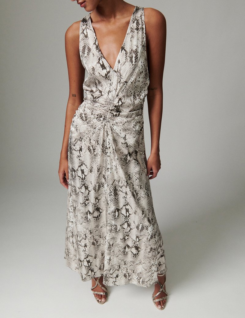 Γυναίκα που φοράει αμάνικο midi φόρεμα με V-λαιμόκοψη και ραβδώσεις, με μπεζ και καφέ φίδι αποτύπωμα, συνδυασμένο με ανάλογα σανδάλια με λουράκια.