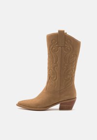 Botte de cowboy en daim marron avec un bout pointu, des coutures décoratives le long de la tige et un talon empilé. Dispose d'une sangle pour un enfilage facile.