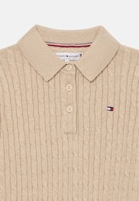 Bežna pletiva polo majica s ovratnikom, tremi gumbi in malo logotipno oznako v rdeči, beli in modri barvi.