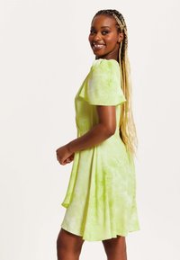 Short-sleeve, knee-length dress in light green with a tie-dye pattern; made from soft fabric with a flowy design. Accentuated shoulder detail.