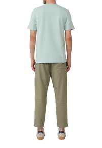 Jasnoniebieska koszulka z krótkim rękawem w połączeniu z luźnymi oliwkowymi spodniami i białymi trampkami z granatowymi akcentami. Prosty, casualowy design.