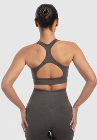 Tummanharmaa urheilullinen crop-top, jossa on racerback-muotoilu ja aukko-ominaisuus, valmistettu sileästä ja joustavasta kankaasta, yhdistetty korkeavyötäröisiin legginsseihin.