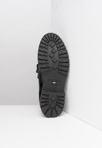 Semelle de chaussure en cuir noir avec un motif de semelle profond, comportant un label en relief avec un logo et un détail du drapeau italien près du talon.
