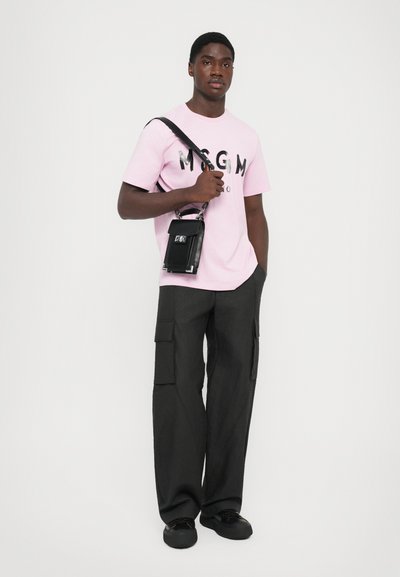 Mand iført en lyserød MSGM T-shirt, sorte cargo bukser, sorte sneakers og bærer en lille sort crossover-taske over den ene skulder.