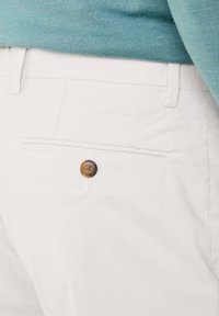 Witte corduroy broek met een horizontaal streeppatroon, voorzien van een achterzak en een ronde bruine knoopaccent.