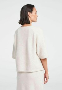 Lys beige sweater med korte, rullede ærmer og en løs pasform. Blød tekstur og minimalistisk design med en rund halsudskæring og sømdetaljer.
