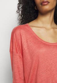 Korallinvärinen kevyt pitkähiha TOPP, jossa on leveä kaula-aukko ja rento istuvuus. Pehmeä pinta, lievä kiilto ja pudotetut olkapääsaumat.