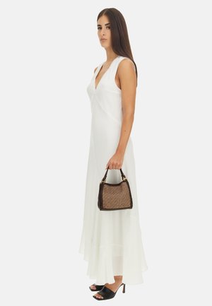 Robe blanche sans manches avec un décolleté profond et une jupe en couches ; tenant un petit sac à main en osier marron avec des accents en cuir noir ; talons ouverts noirs.