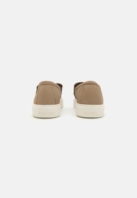 Béžové kožené tenisky s hladkým povrchem, bílou gumovou podrážkou a raženým logem "Calvin Klein" na patě. Jednoduchý a minimalistický design.