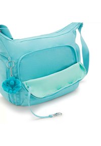 Borse a tracolla turchese realizzata in tessuto morbido, con una tasca frontale, chiusura con zip e un soffice charm come dettaglio su un portachiavi.