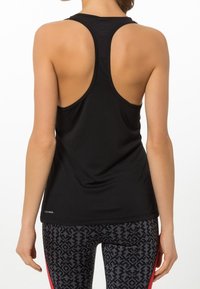 Femme portant un débardeur de sport noir à dos nageur et un legging noir à motifs avec des rayures rouges, vue de dos sur fond blanc.