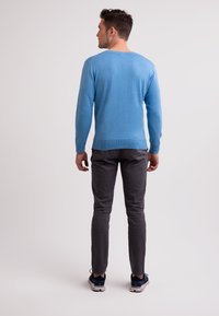 Blå stickad tröja med långa ärmar, rund halsringning och ribbad fåll, tillsammans med slimfit grå byxor och avslappnade sneakers.