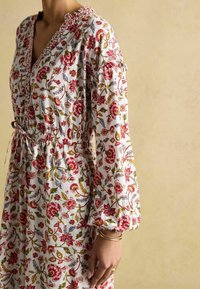 Weißes Blumenkleid mit roten und blauen Mustern, elastischer Taille, V-Ausschnitt und Puffärmeln. Mit Raffung am Ausschnitt.