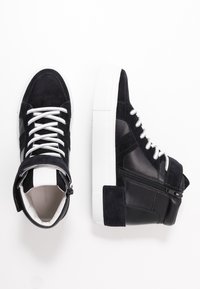 Musta korkeavartiset lenkkarit, jotka on valmistettu nahasta ja mokasta, varustettu valkoisilla nauhoilla, sivuvetoketjulla ja paksulla valkoisella kumipohjalla.