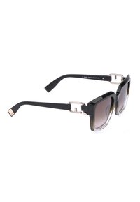 Lunettes de soleil carrées oversize noires avec verres foncés dégradés et accents métalliques géométriques dorés sur les branches.
