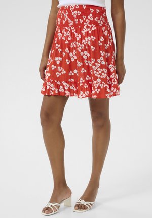 Red floral skirt with a smocked waist, ruffled hem, and scattered white flower patterns. Lightweight fabric enhances flow and movement.