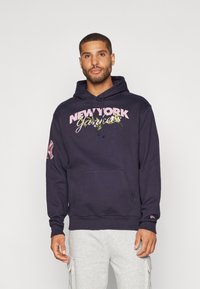 Marineblå hættejakke med frontlomme, prydet med "NEW YORK Yankees" grafik i pink og grøn. Har ribbede manchetter og hætte med snøre.