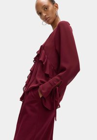 Bordeaux ruffles blouse met lange mouwen, voorzien van een strikdetail bij de mouwen en een vloeiende uitstraling. Soepele textuur.