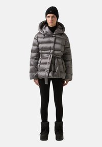 Grå puffjakke med bælte i taljen, hætte og lynlåslommer, kombineret med sorte leggings og støvler. Tekstureret, let materiale.