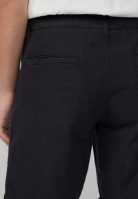 Pantalon noir en tissu lisse, présentant une poche arrière avec un détail de couture subtil. Aucune embellissement ni motif visible.