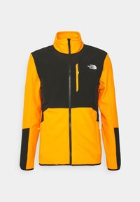 Giacca in pile con colletto alto; parte anteriore e maniche di un arancione vivace, torso e maniche neri; presenta una tasca sul petto con zip e un logo.