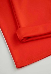 Czerwona tkanina, gładka w dotyku, złożona z czystym wykończeniem. Biała lamówka widoczna wzdłuż jednego brzegu sugeruje możliwość zastosowania warstwowego designu.