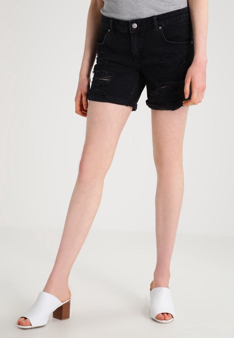 Zwarte denim shorts met verwerkte details, rafelige zomen en een mid-rise pasvorm. Gecombineerd met witte open-toe sandalen met hak.
