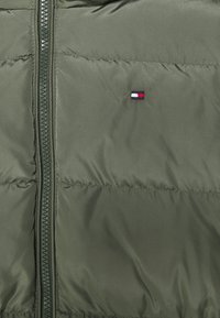 Olivově zelená péřová bunda s předním zipem, prošívanou strukturou a malým logem s červenými, bílými a modrými akcenty.
