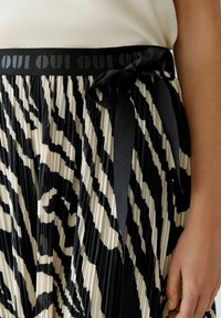 Jupon plissé noir et blanc avec un motif animalier, doté d'une taille noire avec le texte "OUI" et un détail de ruban noué.