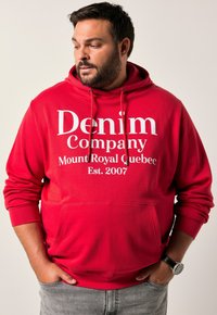 Sudadera roja con bolsillo frontal y capucha con cordón, que presenta texto en blanco que dice "Denim Company Mount Royal Quebec Est. 2007".