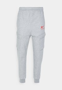 Šedé tepláky s elastickým pasem, zúženými nohavicemi, bočními kapsami a červeným logem Nike na zadní straně.