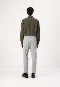 Olive green button-up shirt and light gray tapered trousers with an elastic waistband, paired with black shoes, viewed from the back.