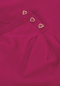 Fuchsia trui met geribbelde halslijn, voorzien van drie gouden hartknopen op de schouder en textuur plissé.