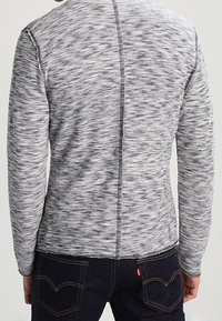 Suéter tejido en gris y blanco con un patrón texturizado, diseño ajustado y una costura central que corre verticalmente por la parte trasera.