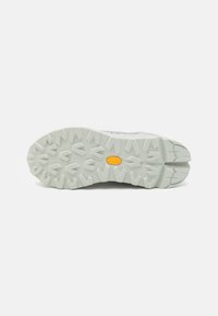 White outsole of a shoe with a rugged design, featuring a prominent tread pattern and a yellow Vibram logo at the center.