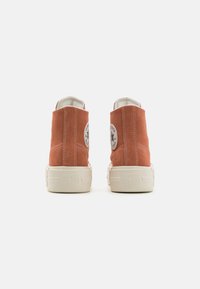 Zapatillas altas de color óxido hechas de ante con suelas blancas de goma. Presenta un parche de logo y costuras en contraste.