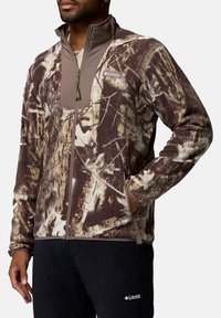 Fleece-Jacke in braunem Camouflage mit einem einfarbigen braunen Brustpanel. Verfügt über einen durchgehenden Reißverschluss, einen stehenden Kragen und seitliche Taschen. Weiche Textur.
