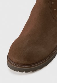 Brown suede ankle boot with a rounded toe, contrasting rubber sole, and visible stitching along the edge. Textured surface with star patterns inside.