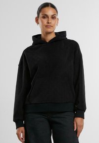 Felpa nera con cappuccio, caratterizzata da un motivo testurizzato, tasca a marsupio e polsini a costine. Il tessuto sembra morbido e caldo. Design cropped.