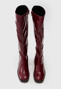 Knee-high burgundy leather boots with a smooth surface, rounded toe, and side zipper; featuring a sleek design and minimalistic accents.