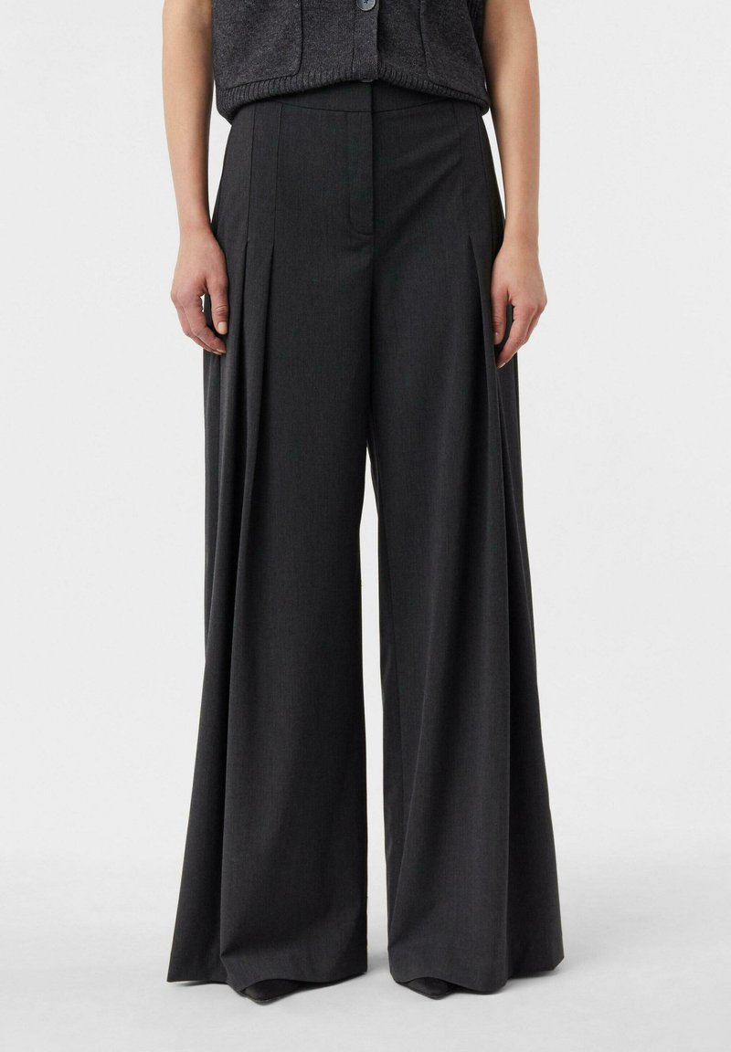 Spodnie o szerokich nogawkach w ciemnoszarym materiale, charakteryzujące się wyraźnymi plisami, wysokim paskiem i dopasowanym krojem. Gładka faktura z delikatnym połyskiem.