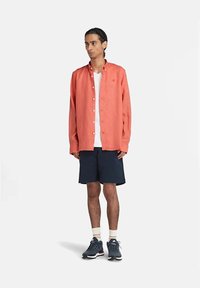 Camicia button-up corallo, t-shirt bianca sotto, pantaloni shorts blu navy, scarpe grigie, con un taglio rilassato e maniche lunghe. Design semplice, senza fantasie.