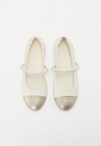Ballerines blanches avec un bout métallique doré, des bords froncés et une sangle décorative en perles au milieu. Texture lisse.