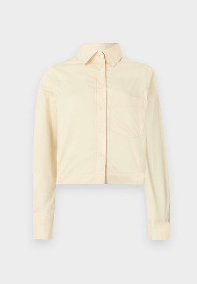 Przycięta, długorękawowa koszula z jasnopłótnowego bawełnianego materiału. Posiada standardowy kołnierzyk, zapięcie na guziki z przodu oraz jedną kieszeń na piersi.