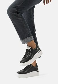 Sneakers in pelle nera con suola platform bianca, dotati di lacci rotondi, logo laterale e dettagli di cucitura sottili.