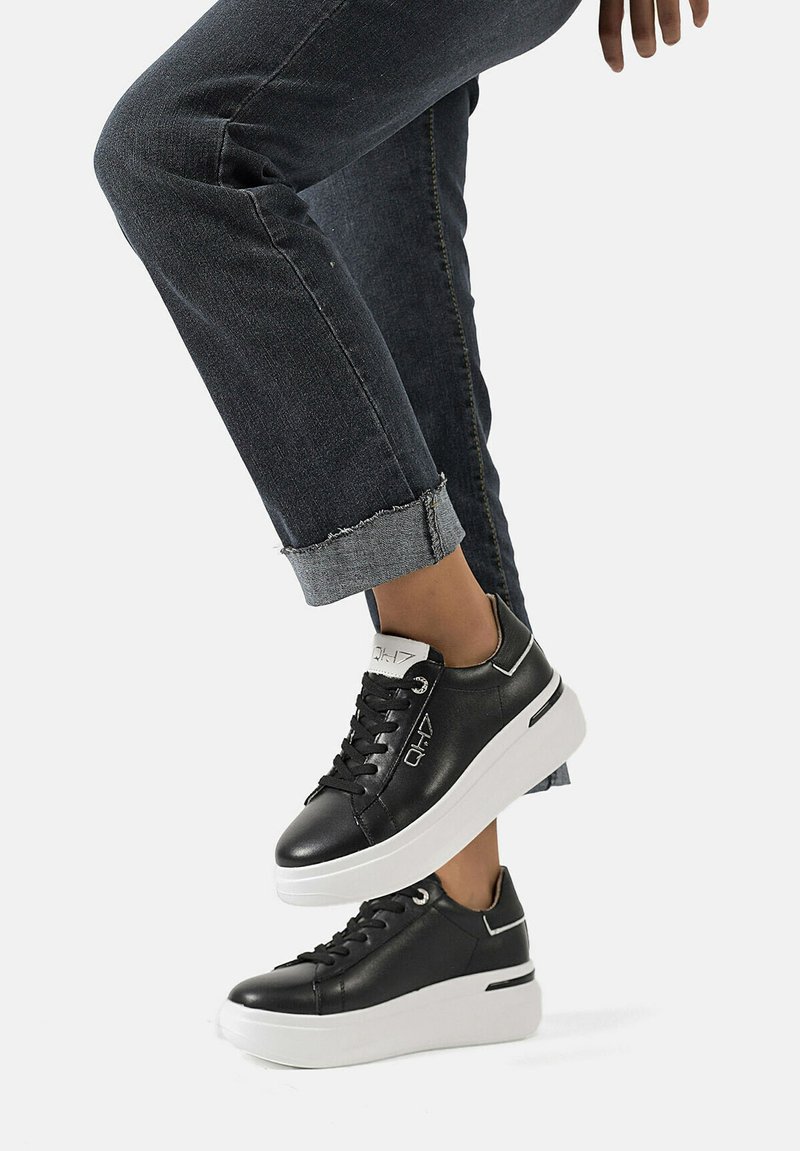 Sneakers in pelle nera con suola platform bianca, dotati di lacci rotondi, logo laterale e dettagli di cucitura sottili.