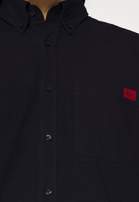 Donkerblauw overhemd met knopen en een klassieke kraag, met een borstzak en een rood Hugo-logo patch. Glad, gestructureerd materiaal.