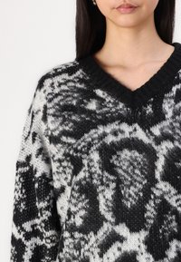 Maglione a righe bianche e nere con scollatura a V, texture lavorata a maglia e vestibilità ampia, che mette in risalto il contrasto audace e il materiale morbido.