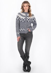 Modrá a bílá pletená kardigan s aztéckými vzory, zapínání na knoflíky, dlouhé rukávy, doplněná šedými skinny džíny a černými vysokými botami po kolena.